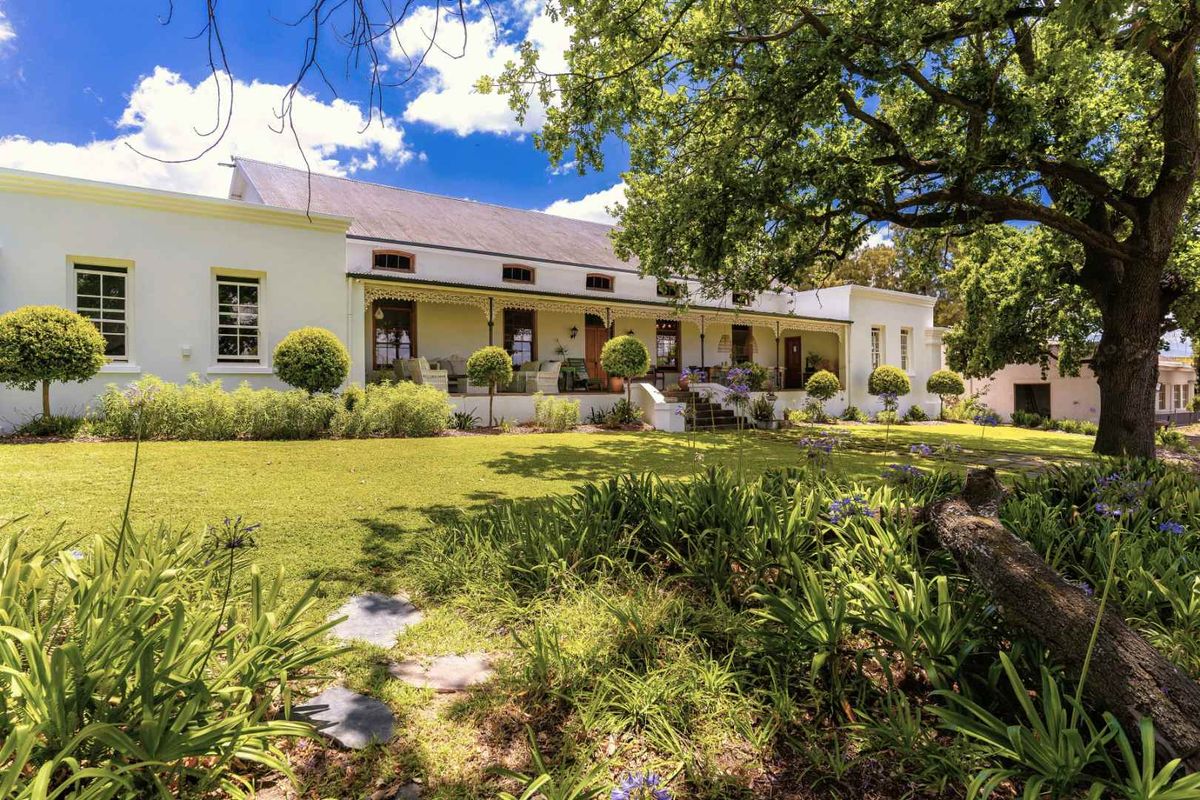 A charming farmhouse exterior featuring a covered veranda, manicured lawn, and mature trees, showcasing classic architectural style and well-maintained grounds.