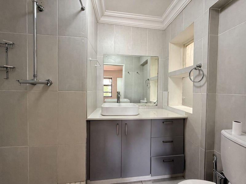 A modern bathroom featuring a vanity cabinet with a countertop basin, tiled walls, built-in shelving, and a wall-mounted shower fixture.