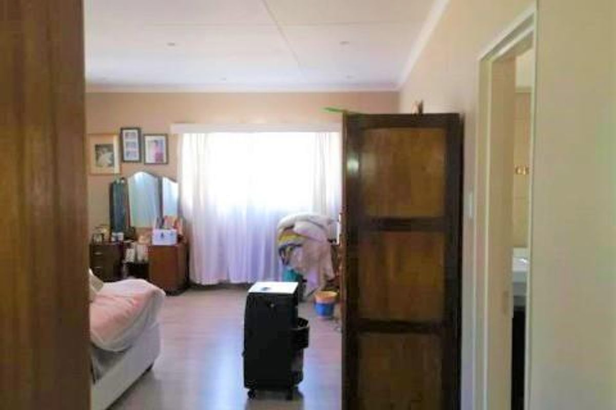 A view into a bedroom featuring light-toned laminate flooring, neutral walls, and an adjacent doorway leading to a bathroom.