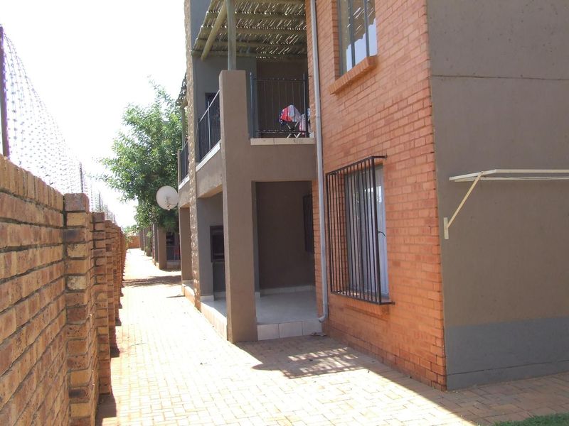 Rear view of the apartment complex featuring a paved walkway, brick boundary wall with security fencing, and balconies with security bars.