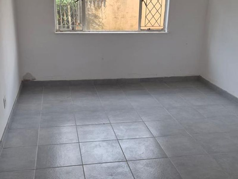 An empty bedroom featuring grey tiled flooring, a ceiling fan, and a window with security bars.