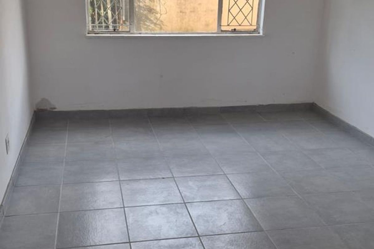 An empty bedroom featuring grey tiled flooring, a ceiling fan, and a window with security bars.