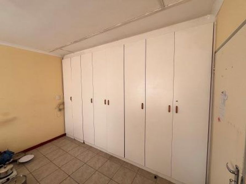 A bedroom featuring extensive built-in cupboards and tiled flooring, currently vacant and ready for refurbishment.