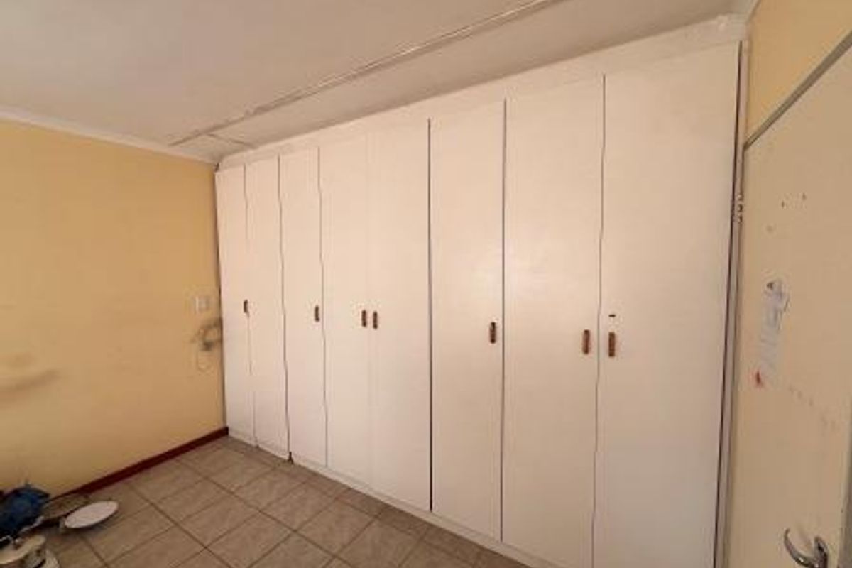 A bedroom featuring extensive built-in cupboards and tiled flooring, currently vacant and ready for refurbishment.