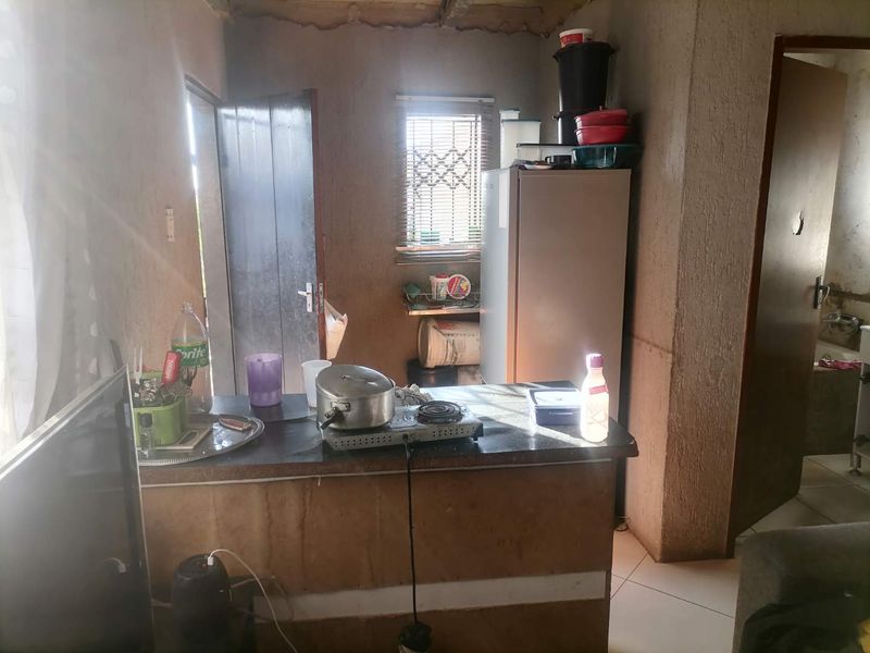 A compact kitchen area featuring a basic counter, tiled flooring, and window with security bars, requiring significant cosmetic updates and finish improvements.