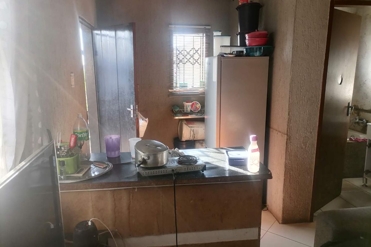 A compact kitchen area featuring a basic counter, tiled flooring, and window with security bars, requiring significant cosmetic updates and finish improvements.