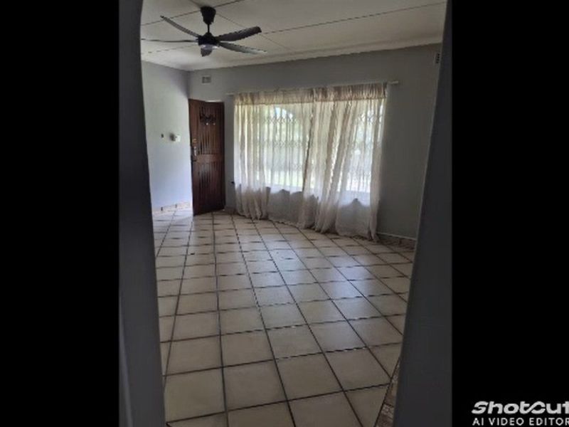 An empty living room featuring tiled flooring, a ceiling fan, and window security bars, viewed through a doorway.