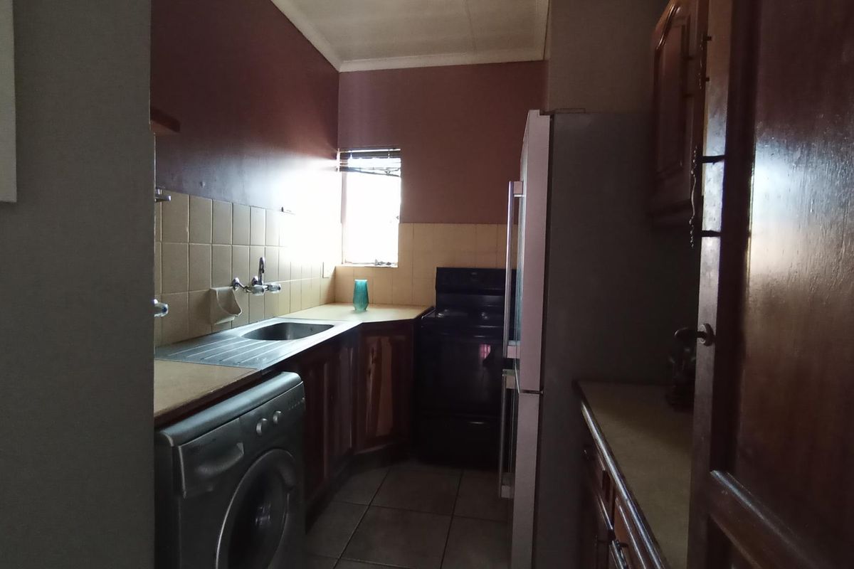 A compact kitchen featuring dated wooden cabinetry, tiled backsplash, stainless steel sink, and space for a freestanding stove and laundry appliance.