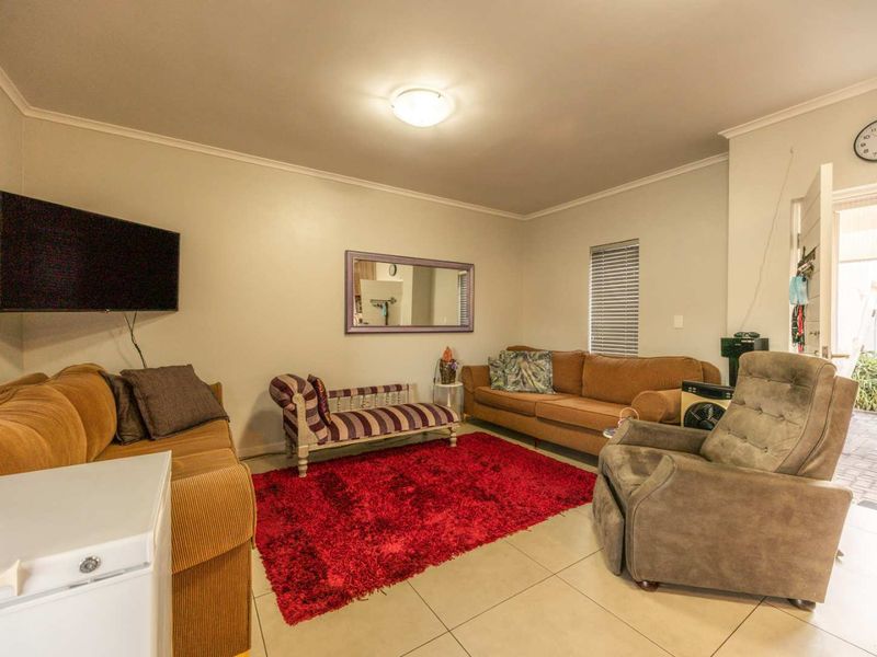 A comfortable living room featuring neutral tiled flooring, ceiling lighting, and venetian blinds, providing a functional and well-lit space for relaxation.