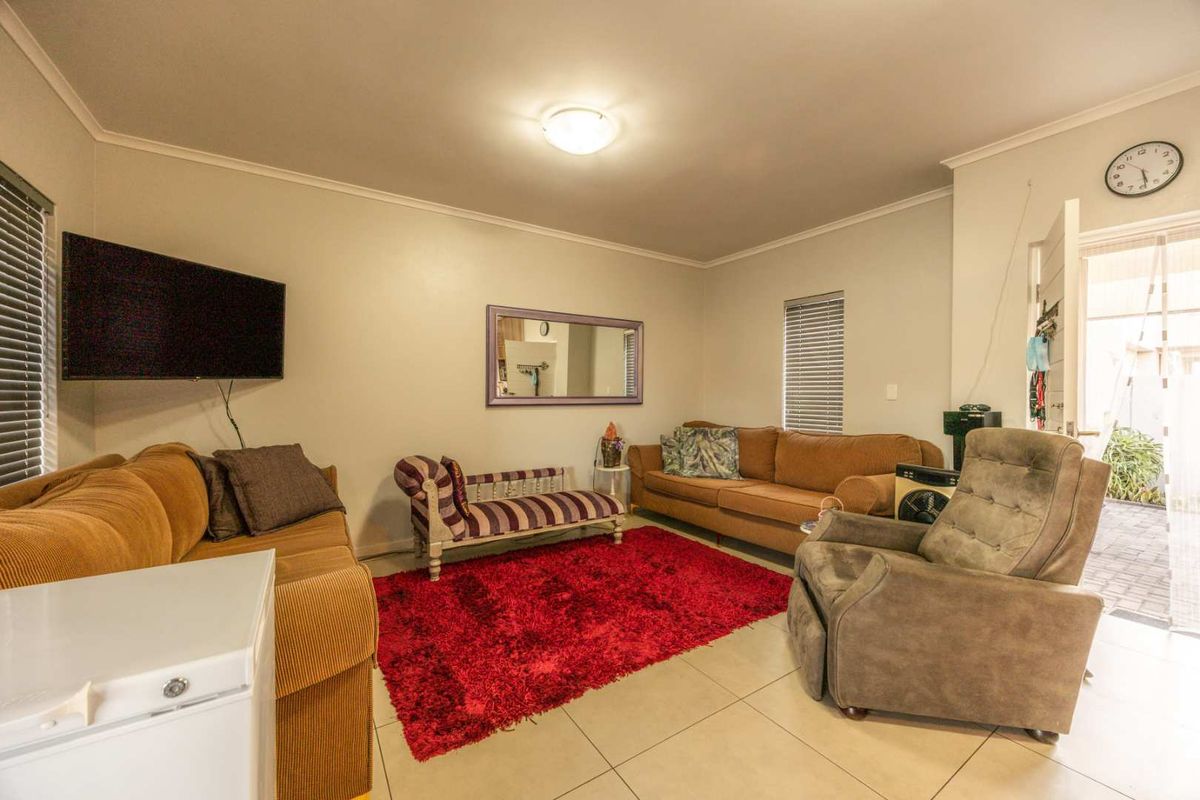 A comfortable living room featuring neutral tiled flooring, ceiling lighting, and venetian blinds, providing a functional and well-lit space for relaxation.