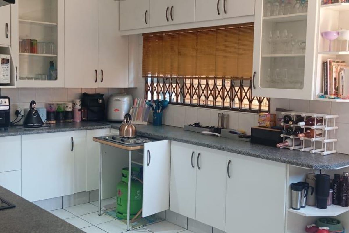 Functional kitchen featuring white cabinetry, laminate countertops, tiled flooring, and a window with security bars, providing a practical workspace for daily meal preparation.