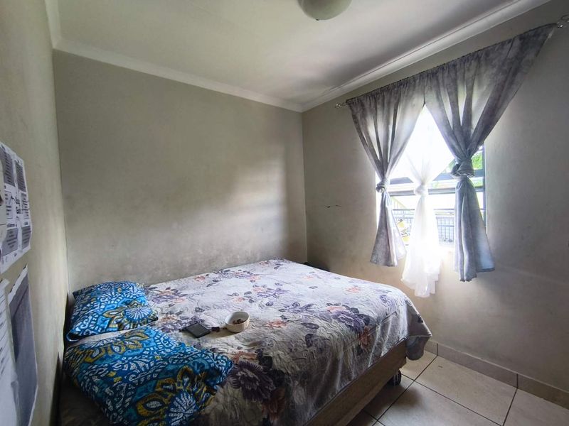 A compact bedroom featuring tiled flooring and a window with natural light, requiring cosmetic updates to the wall finishes.