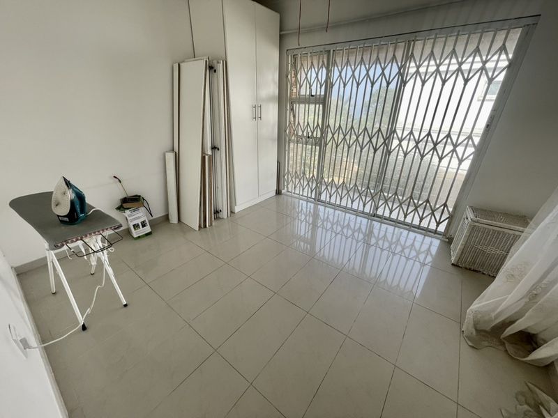 A bright, empty bedroom featuring tiled flooring, built-in cupboards, and a sliding door with a security gate leading to the exterior.