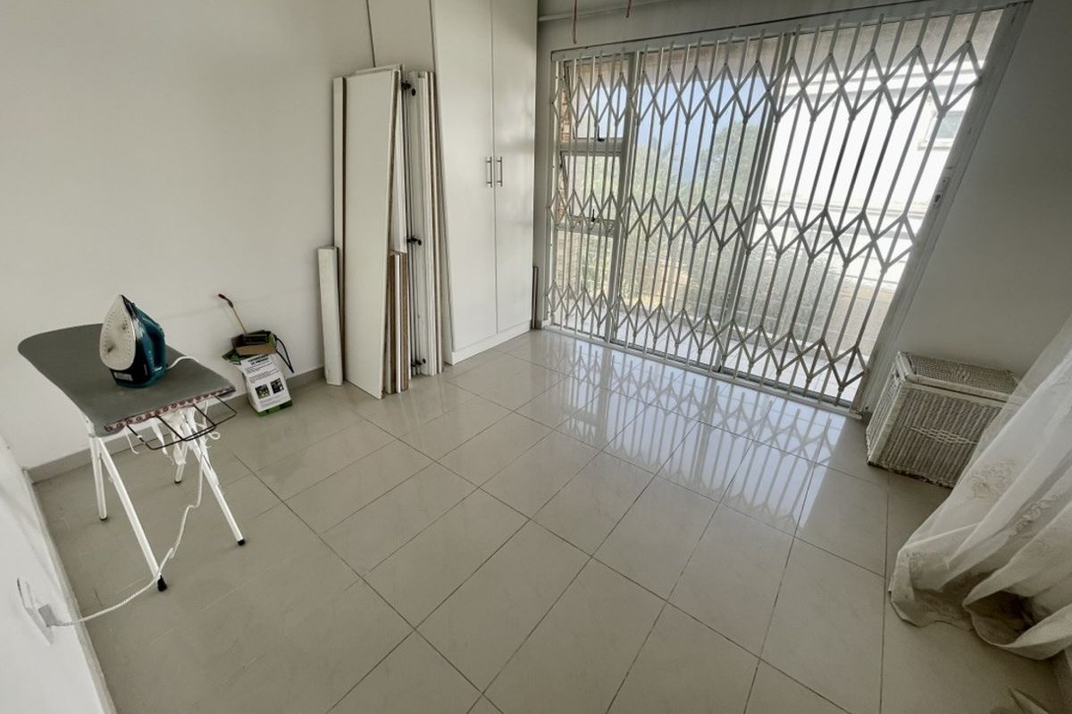 A bright, empty bedroom featuring tiled flooring, built-in cupboards, and a sliding door with a security gate leading to the exterior.