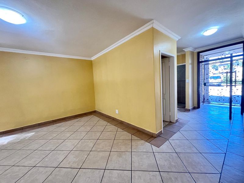An empty, open-plan living area featuring neutral tiled flooring, crown molding, and a secure metal entrance gate.