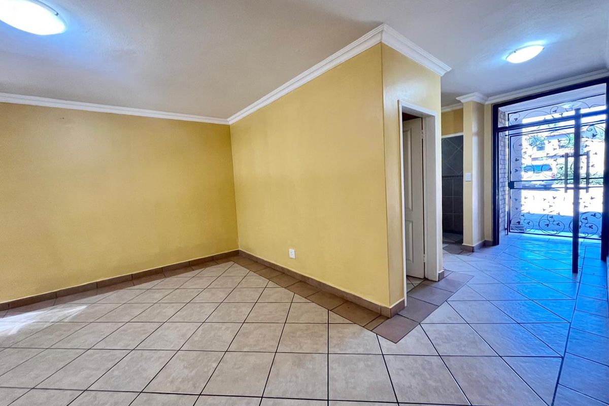 An empty, open-plan living area featuring neutral tiled flooring, crown molding, and a secure metal entrance gate.
