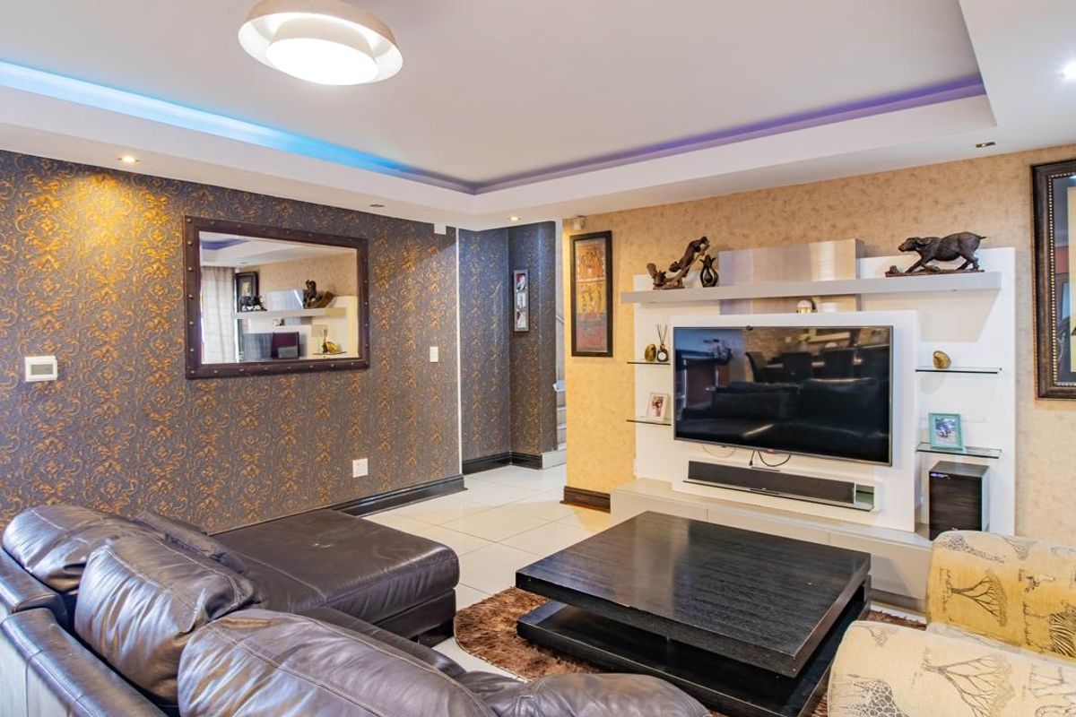 A living room featuring a built-in media wall unit, recessed ceiling lighting with ambient LED strips, and tiled flooring.