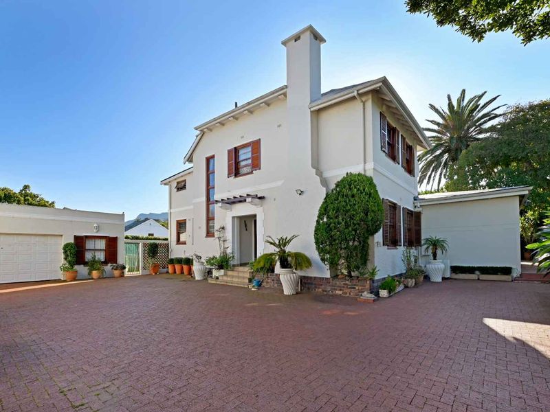 A well-maintained two-story house featuring a brick-paved driveway, attached garage, and classic architectural details including shutters and a prominent chimney.