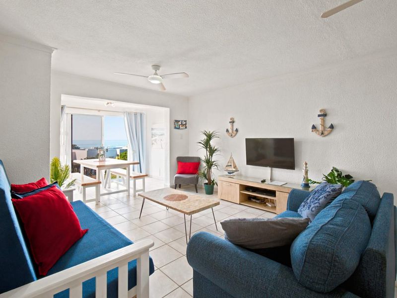 Bright living room featuring tiled flooring, a ceiling fan, and sliding glass doors leading to a balcony with ocean views.