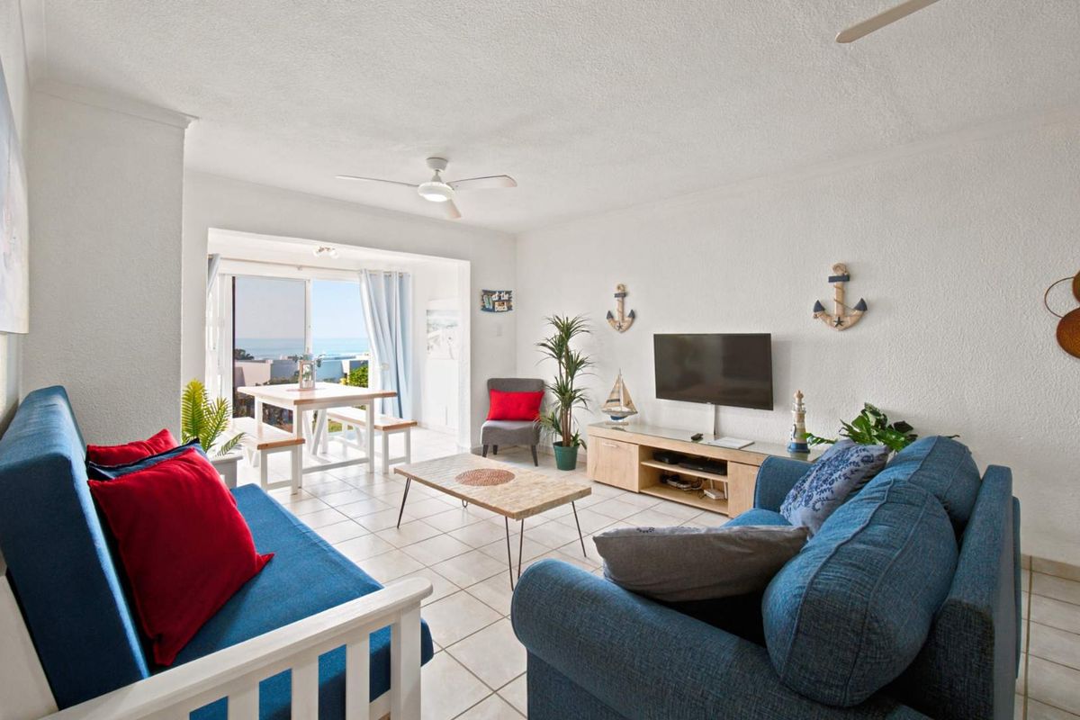 Bright living room featuring tiled flooring, a ceiling fan, and sliding glass doors leading to a balcony with ocean views.
