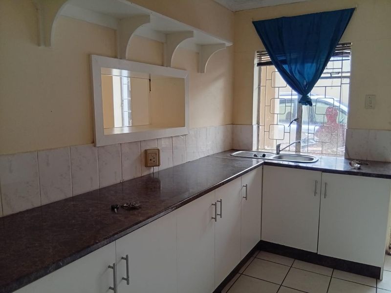 A functional kitchen area featuring laminate countertops, built-in cabinetry, a stainless steel sink, and tiled flooring with security bars on the window.