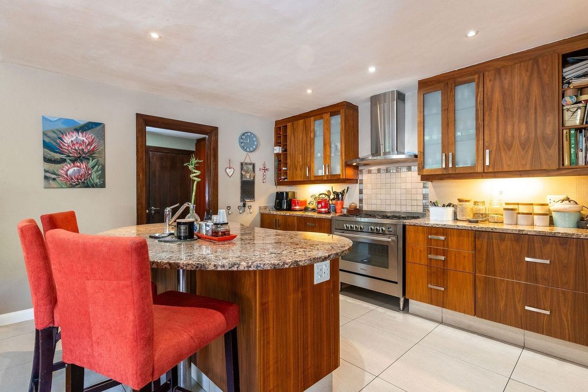 A well-appointed kitchen featuring warm wood cabinetry, granite countertops, a central island, and stainless steel appliances including a gas range and extractor fan.