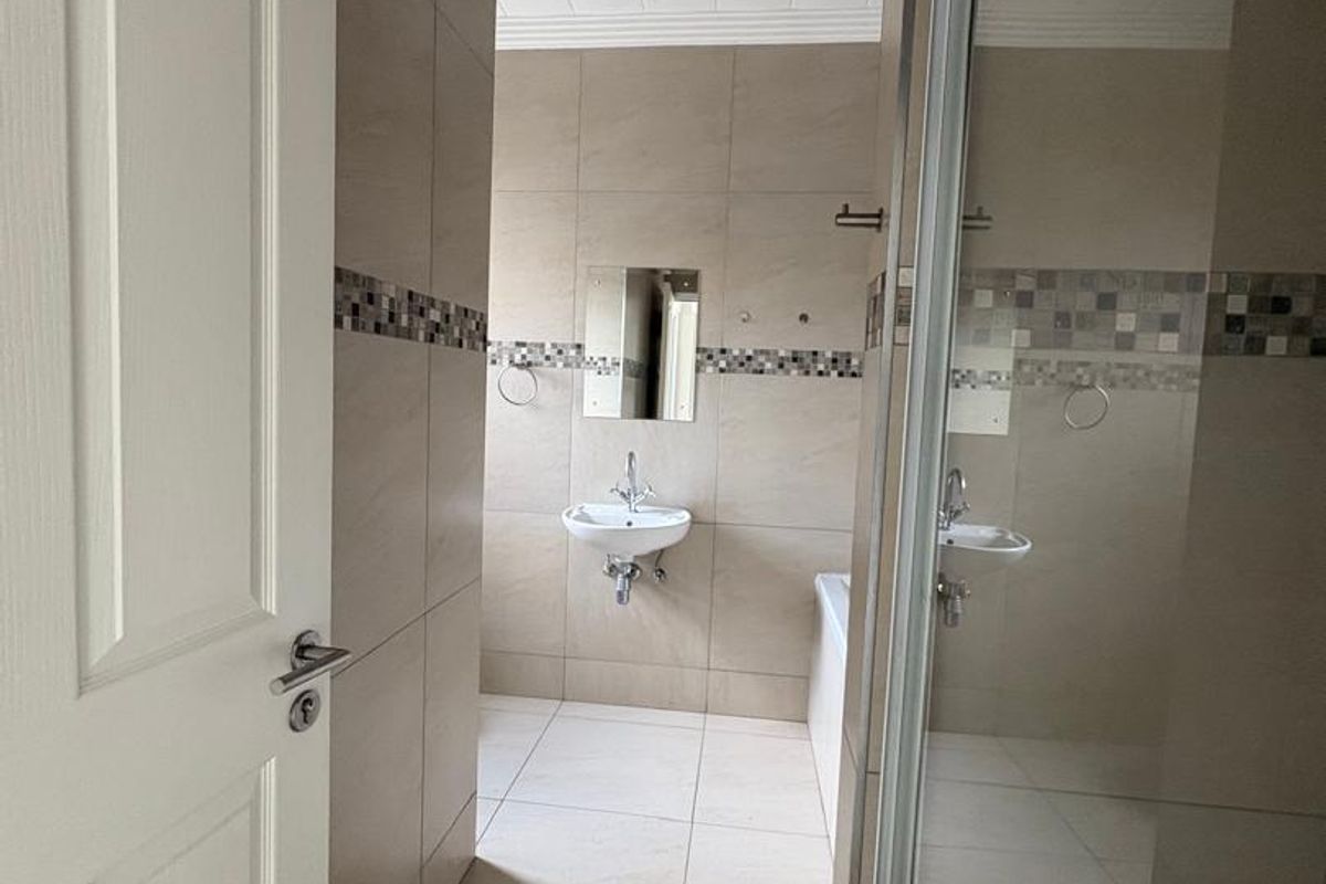 A modern bathroom featuring neutral wall tiles, a glass-enclosed shower, a wall-mounted basin, and a bathtub.