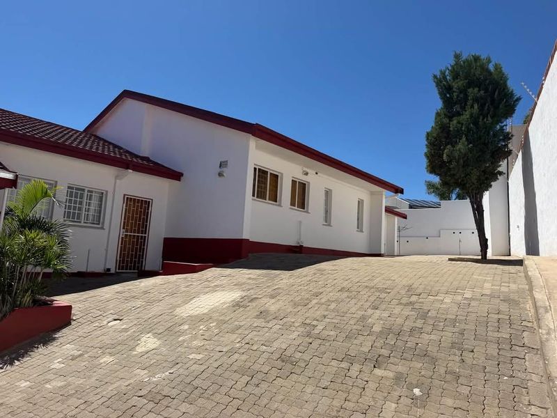 Front exterior view of the property featuring a paved driveway, white facade with red trim, and secure perimeter walling.