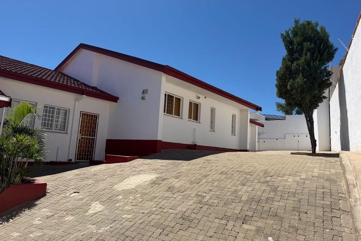Front exterior view of the property featuring a paved driveway, white facade with red trim, and secure perimeter walling.