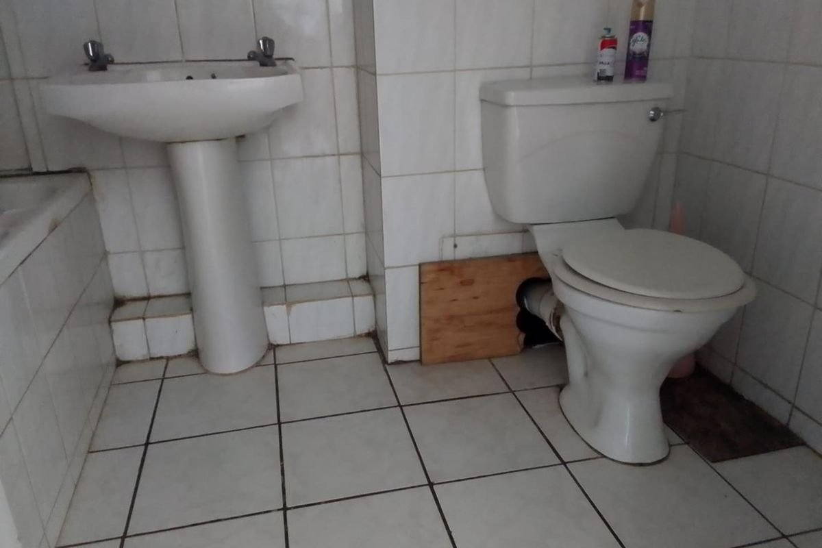 A dated bathroom featuring a pedestal basin and toilet with visible plumbing repairs and worn tiling throughout.