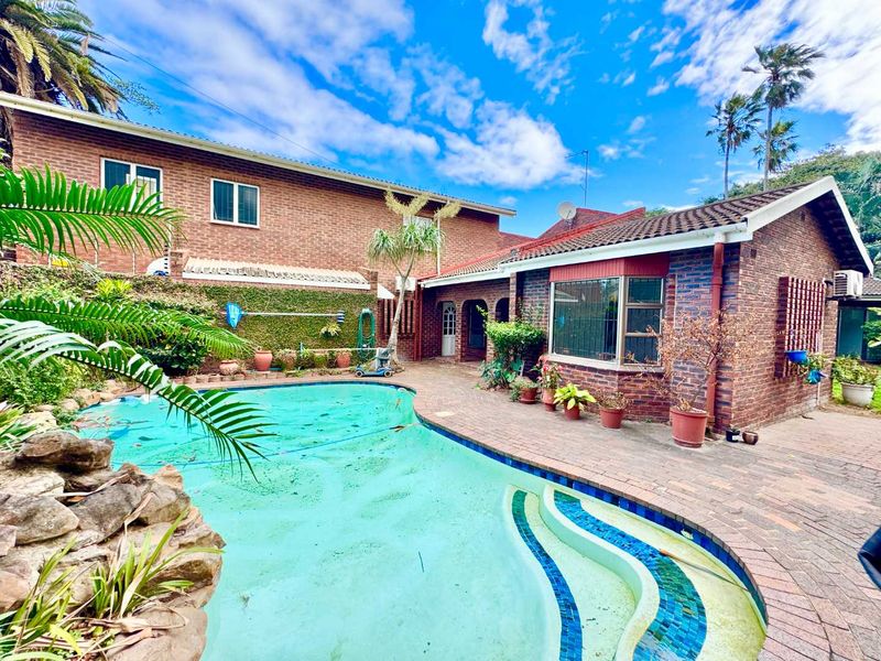 Rear exterior view featuring a swimming pool, brick house facade, and paved patio area.