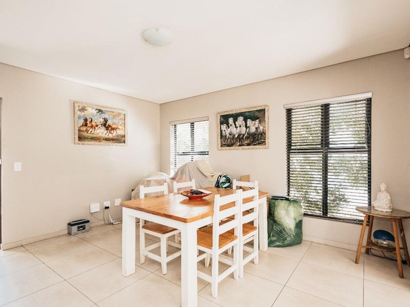 A dining room featuring neutral tiled flooring, large windows with venetian blinds, and a central ceiling light fixture.