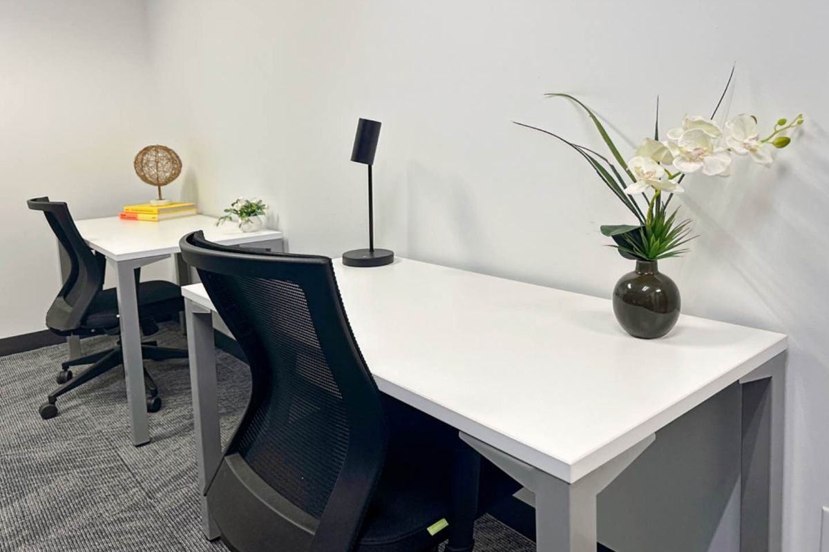A clean and modern office space featuring neutral walls, carpeted flooring, and functional workspace arrangements.