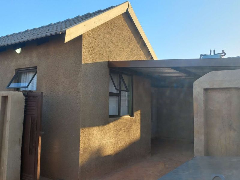Rear view of the property featuring a textured plaster facade, tiled roof, covered patio area, and a precast concrete boundary wall.