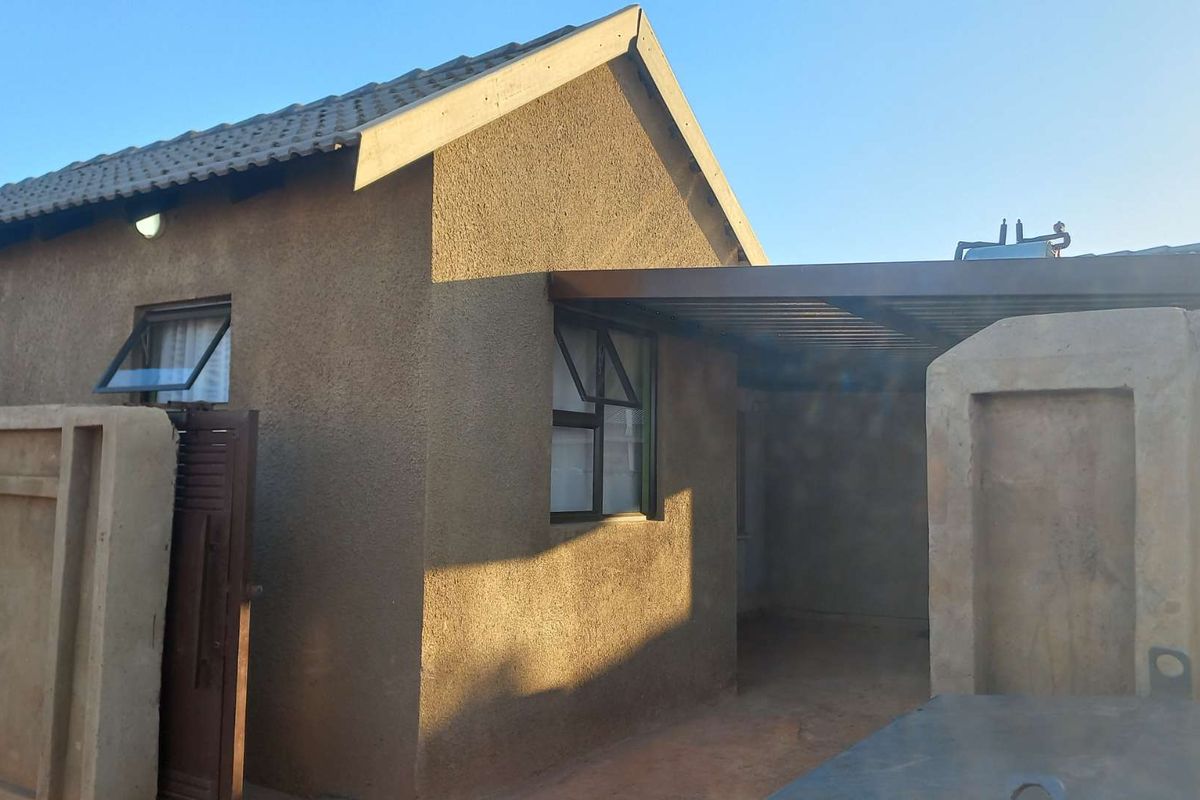 Rear view of the property featuring a textured plaster facade, tiled roof, covered patio area, and a precast concrete boundary wall.