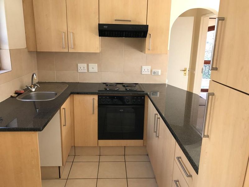 A functional kitchen featuring light wood cabinetry, dark granite countertops, built-in oven and hob, and tiled flooring.