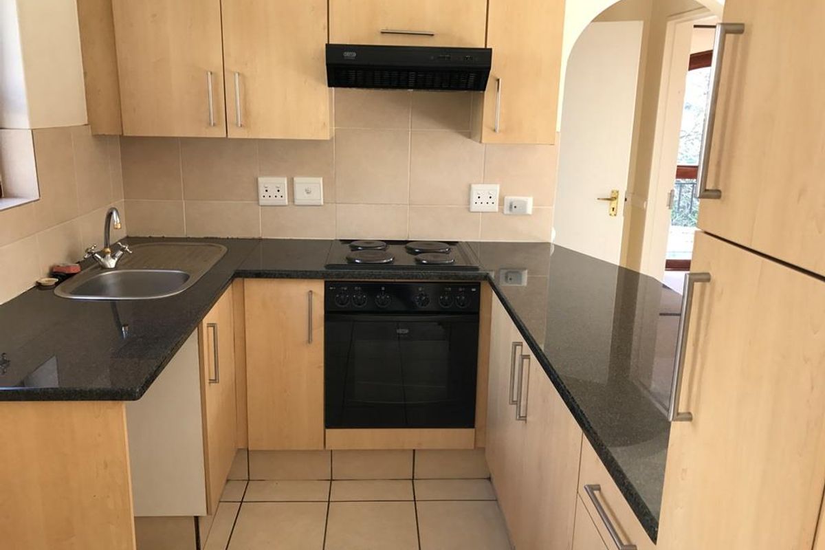 A functional kitchen featuring light wood cabinetry, dark granite countertops, built-in oven and hob, and tiled flooring.