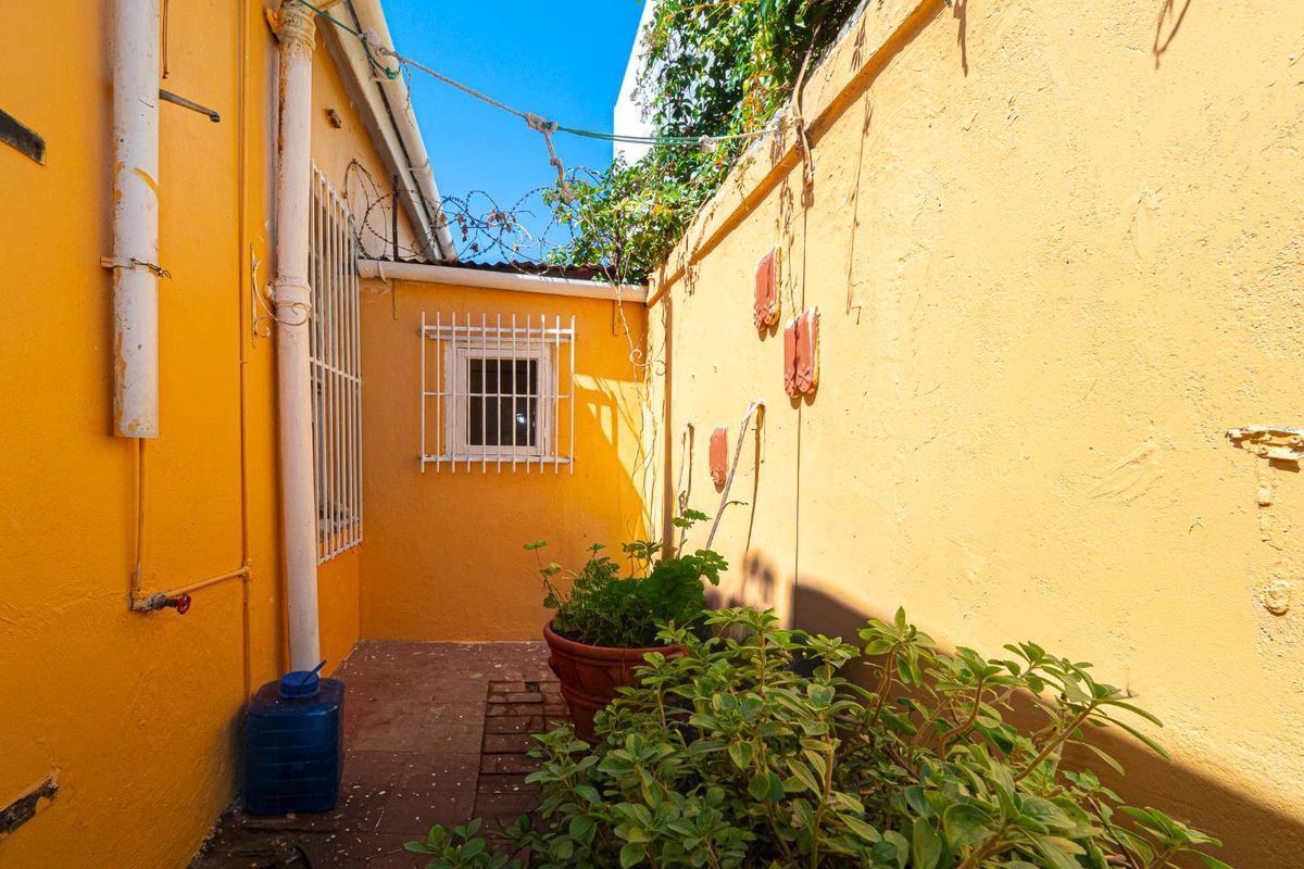 A narrow exterior side passage or courtyard area featuring yellow painted walls, security bars on the window, and a drainage downpipe.