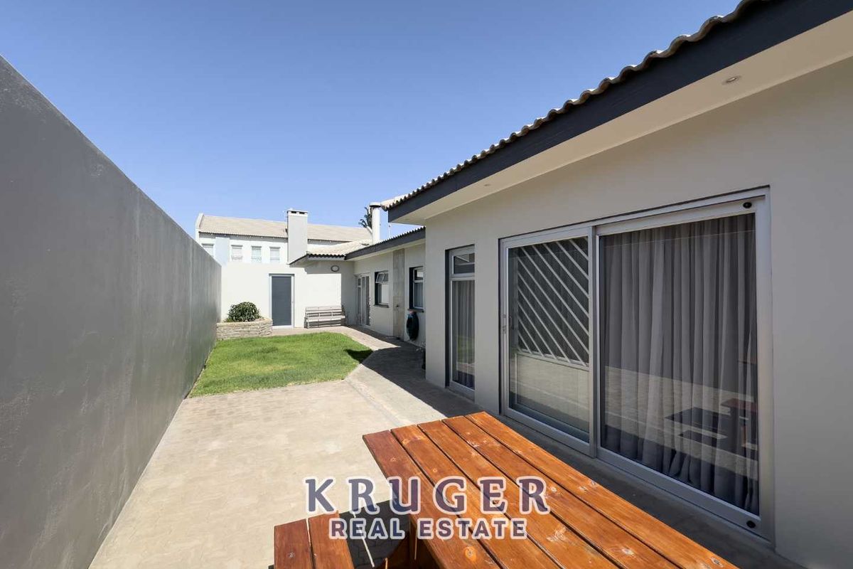A well-maintained rear courtyard featuring a paved patio area, a small lawn, and sliding glass doors providing seamless indoor-outdoor access.