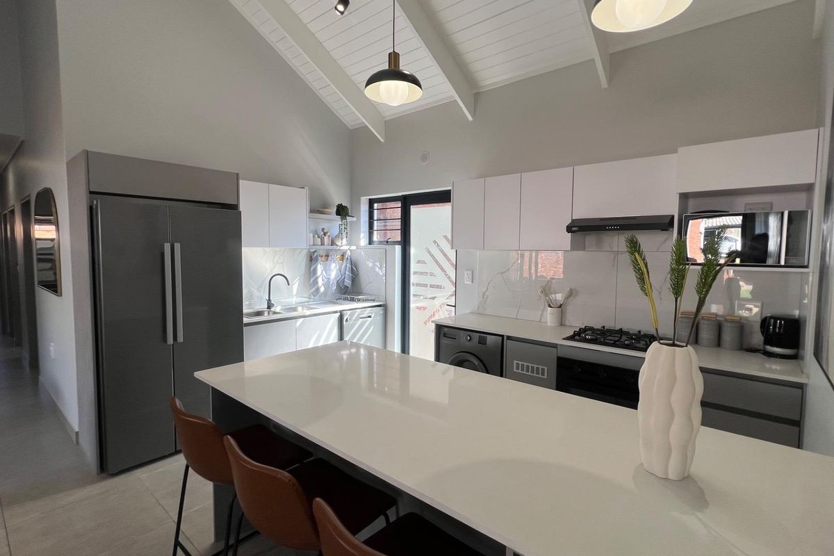 Modern kitchen featuring a central island, quartz countertops, built-in gas hob, oven, and sleek cabinetry under a high vaulted ceiling.