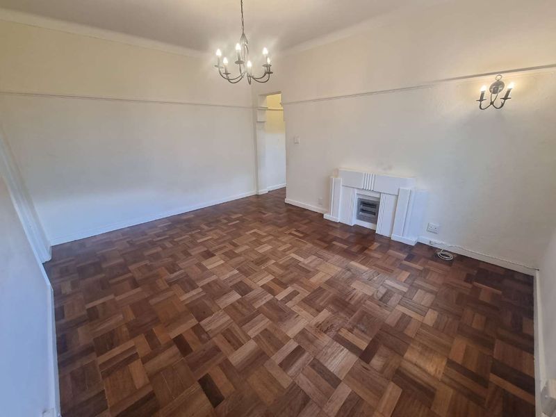 Spacious living room featuring original parquet flooring, a decorative fireplace mantel, and classic period details including picture rails and crown molding.