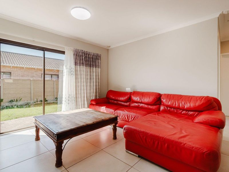 A bright living room featuring tiled flooring and a large sliding glass door providing direct access to the rear garden area.