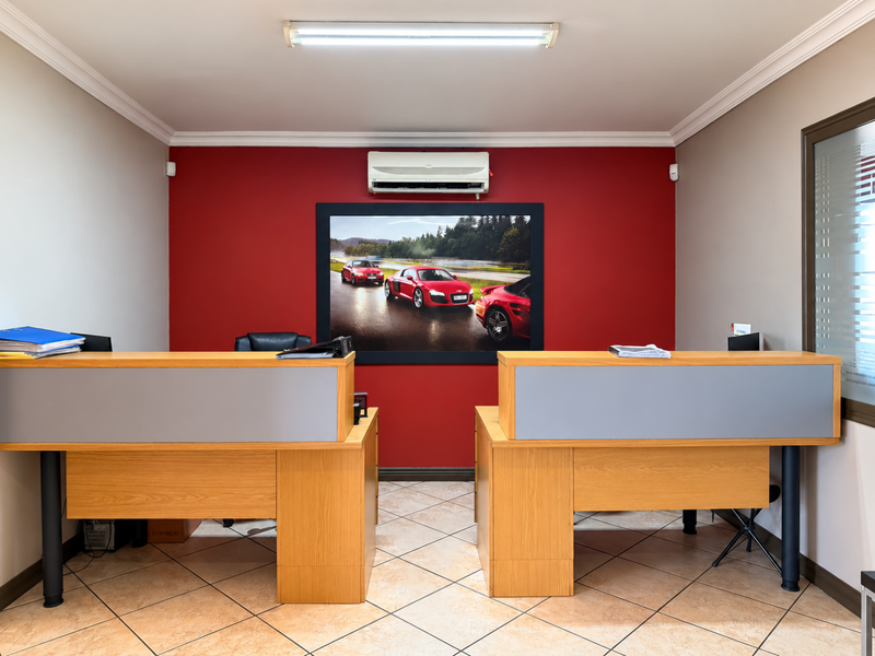 A professional office space featuring dual built-in reception desks, tiled flooring, and a wall-mounted air conditioning unit against a red accent wall.
