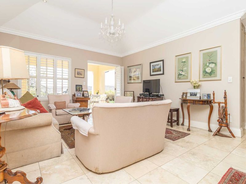 Spacious living room featuring vaulted ceilings, crown molding, elegant tiled flooring, and plantation shutters, with direct access to an outdoor patio area.