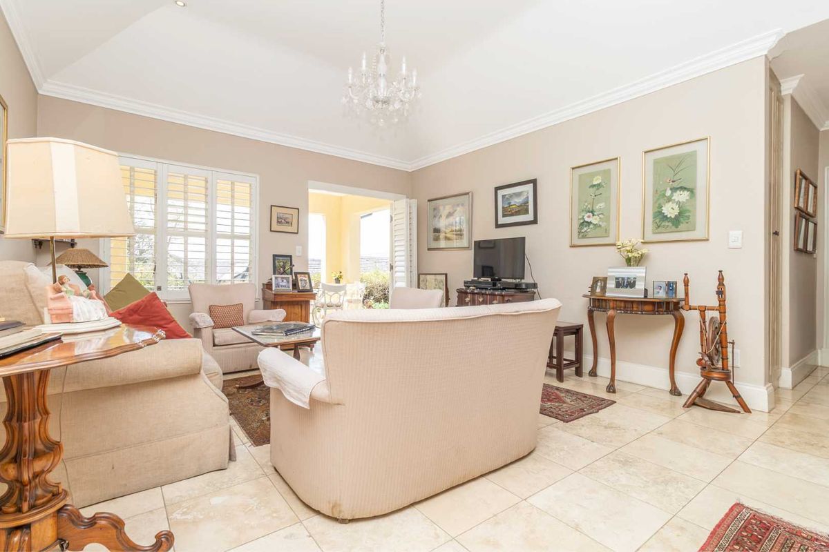 Spacious living room featuring vaulted ceilings, crown molding, elegant tiled flooring, and plantation shutters, with direct access to an outdoor patio area.