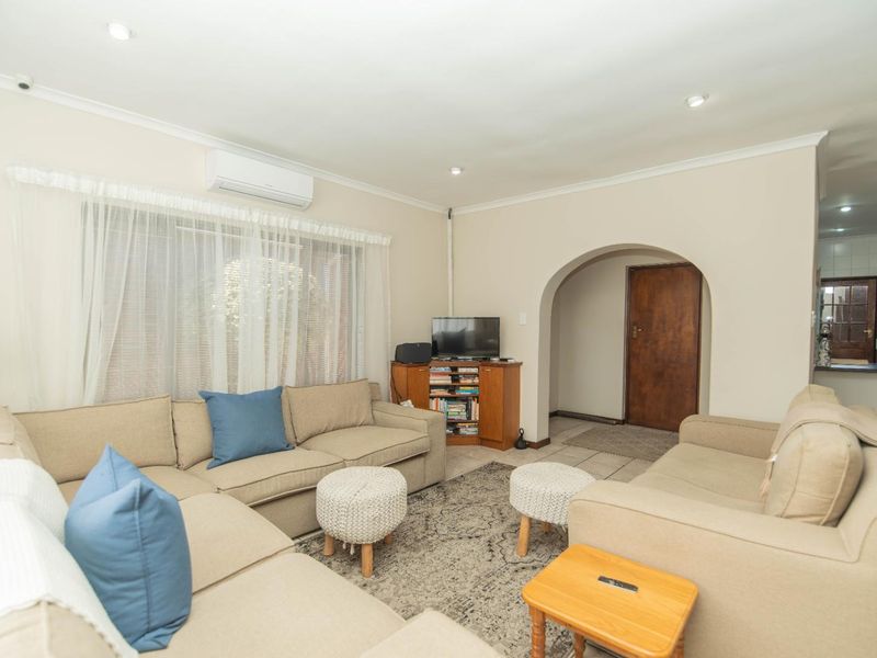 A comfortable living room featuring tiled flooring, recessed downlighting, and a classic archway leading to an adjacent space, equipped with a wall-mounted air conditioning unit.