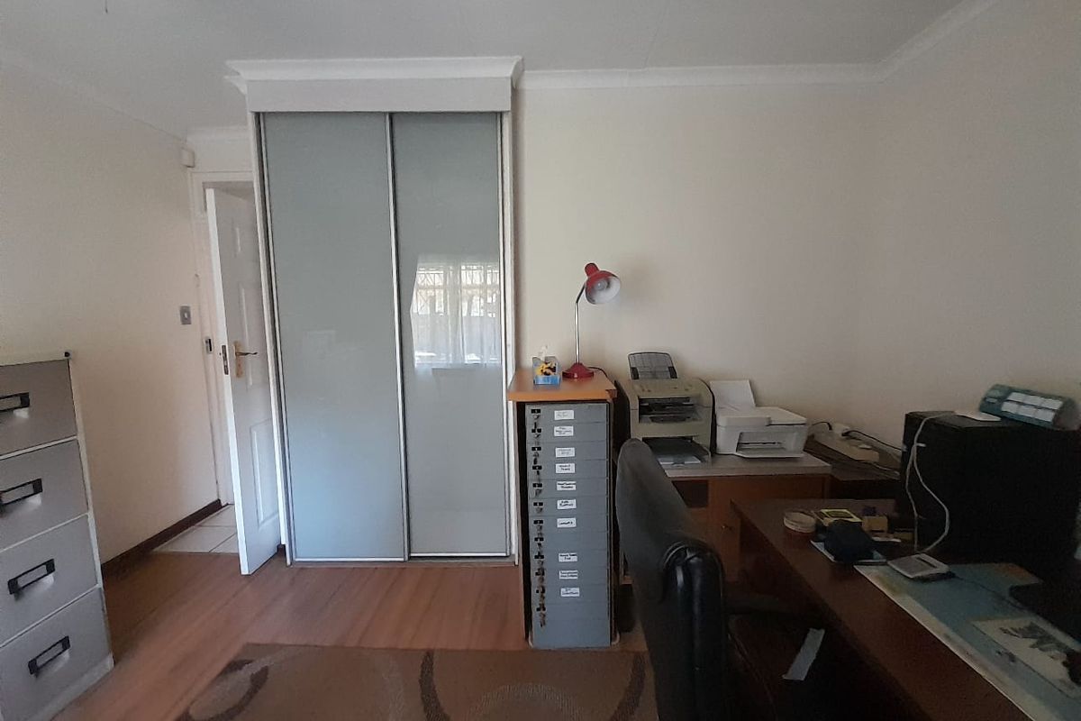 A functional bedroom featuring laminate flooring and a built-in sliding door wardrobe, currently utilized as a home office space.