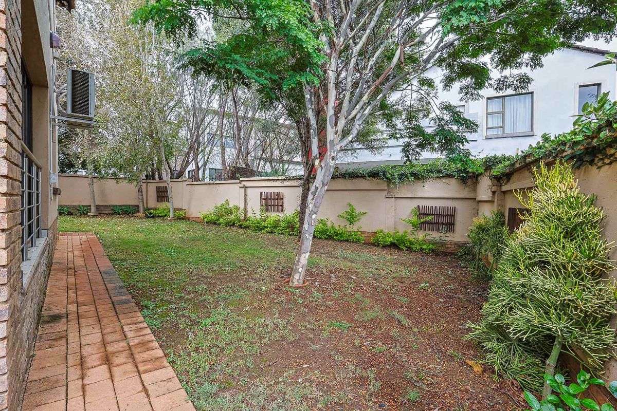 A private rear garden featuring a brick-paved walkway, established trees, and a perimeter boundary wall.