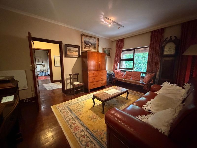 A cozy living room featuring polished hardwood flooring, cove molding, and natural light through a large window, providing a warm and traditional atmosphere.