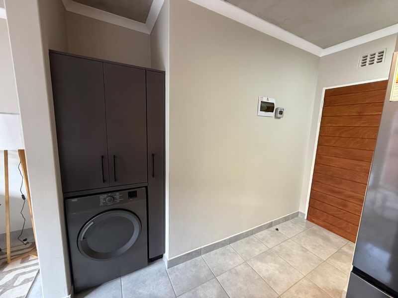 A clean and functional laundry area featuring built-in cabinetry, tiled flooring, and a solid timber door.